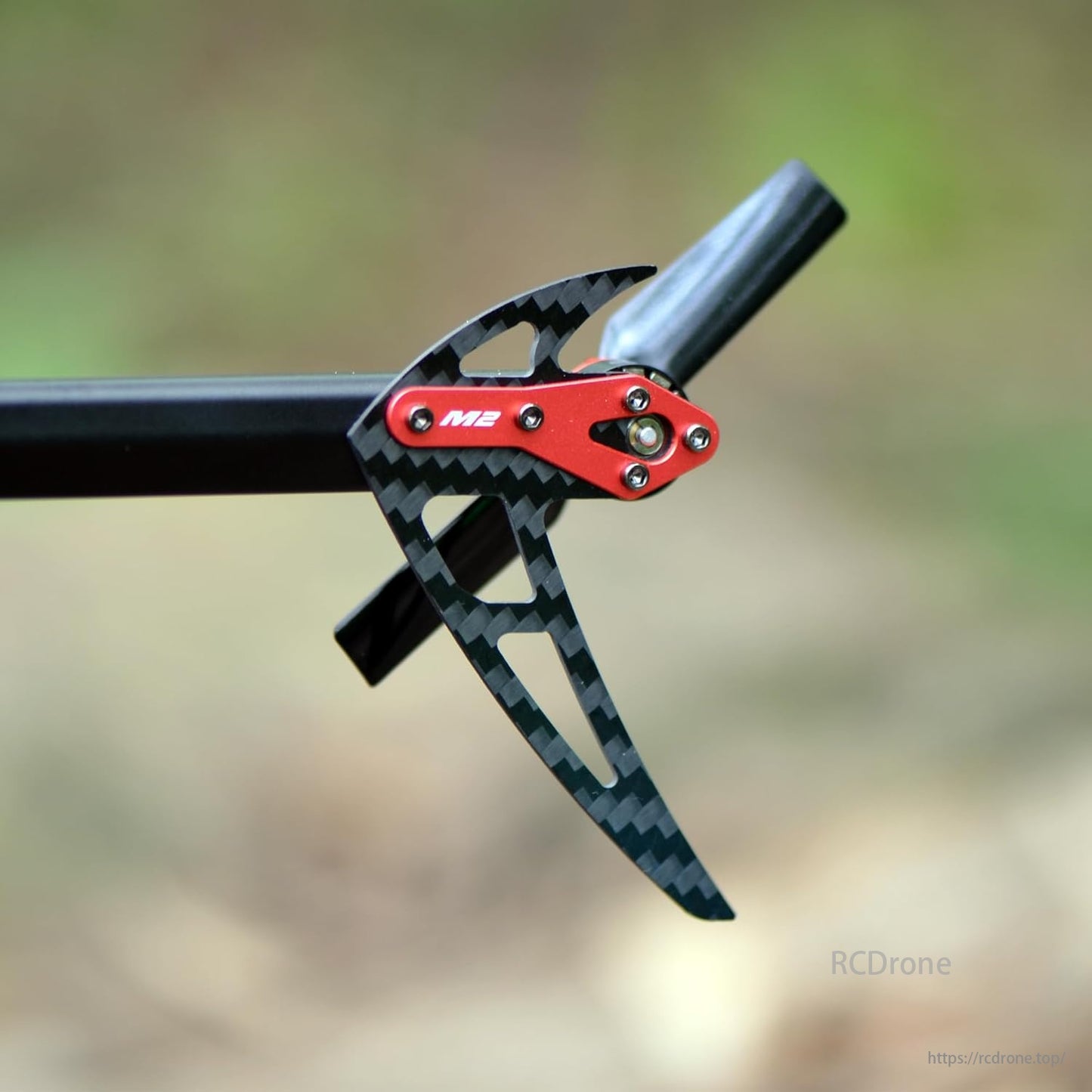 OMPHOBBY M2 V2 RC Helicopter, Red and black mechanical component with "M2" label, attached to a cylindrical structure.