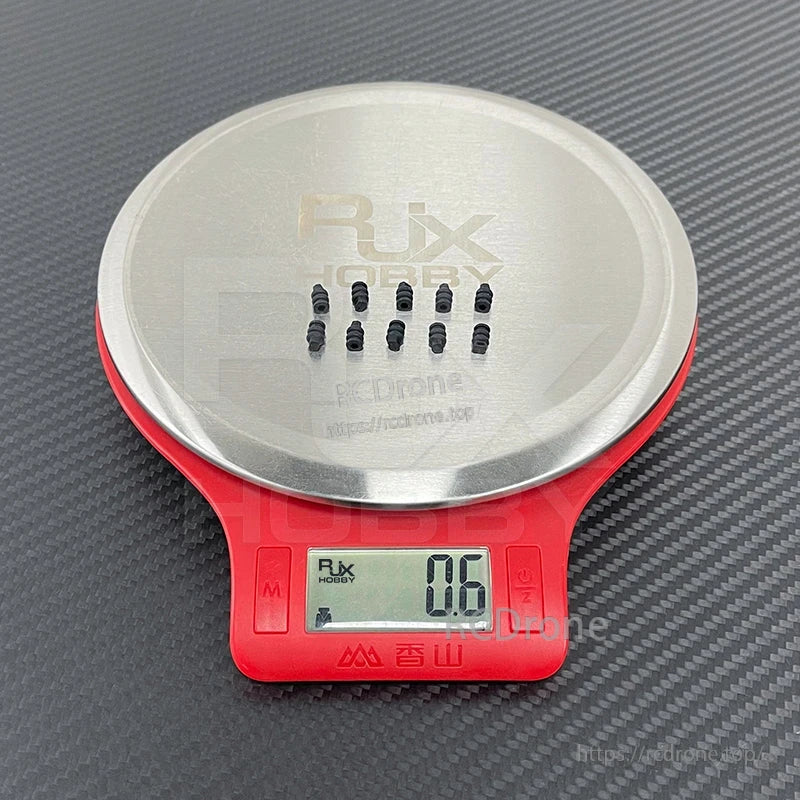 RJX 50pcs Gimbal Rubber Damping Ball, Small black RJX gimbal rubber damping balls on a digital scale reading 0.6 g