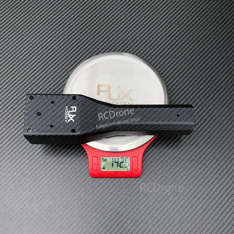 RJXHOBBY carbon fiber UAV arm on digital scale reading 142.5 g, with multiple mounting holes and matte carbon texture.
