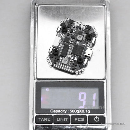 Flywoo GOKU HD745 EVO 20x20 AIO flight controller on a digital scale, showing about 9 g weight and USB port