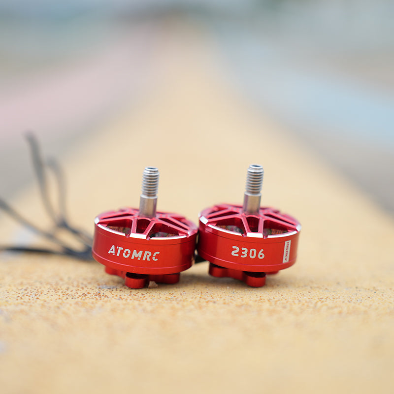 Out-of-focus close-up of a red brushless drone motor on a sandy surface with wires in the background