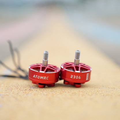 Out-of-focus close-up of a red brushless drone motor on a sandy surface with wires in the background