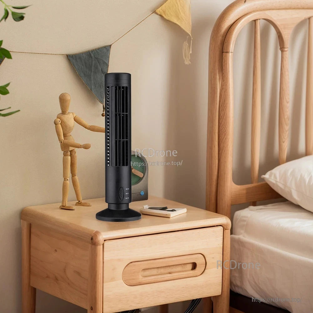 Black mini tower fan on wooden bedside table next to bed, compact desktop placement