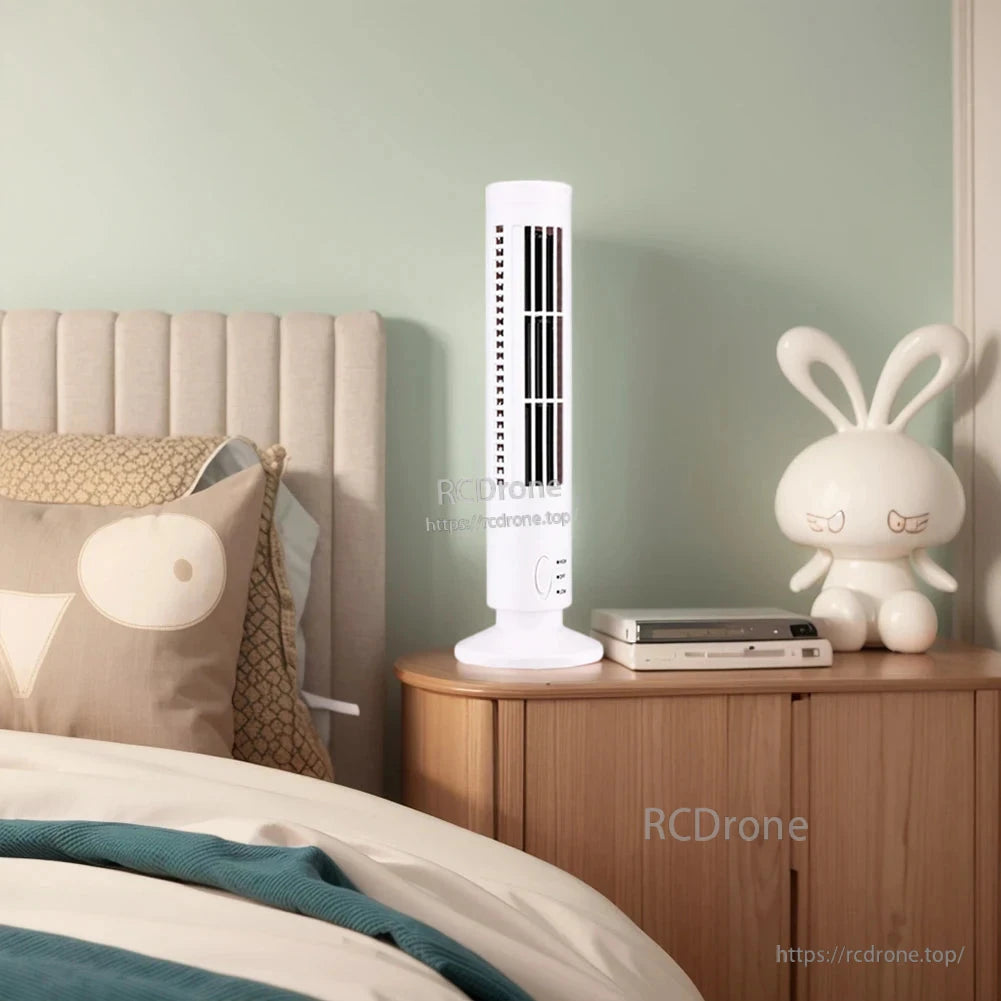 White tower fan on cabinet beside bed, slim vertical design for bedroom nightstand use