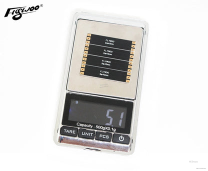 Four Flywoo 9x40mm FPV drone frame arm boards with solder pads displayed on a digital pocket scale