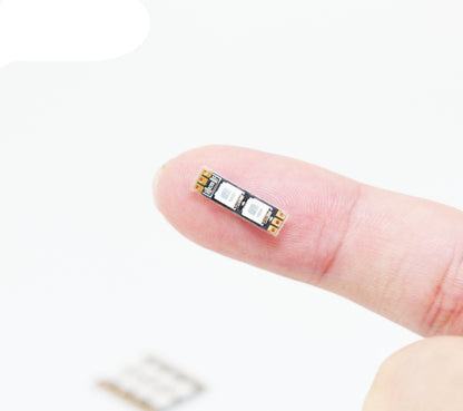 Small FLYWOO frame arm LED board light with two SMD LEDs and solder pads, shown on a fingertip