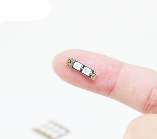 Small FLYWOO frame arm LED board light with two SMD LEDs and solder pads, shown on a fingertip
