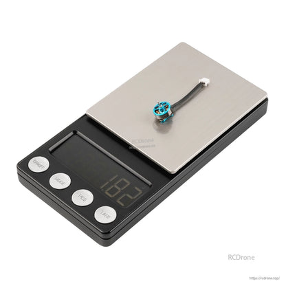 Blue micro brushless motor on digital scale, weight display showing 1.82 g with lead wire and connector