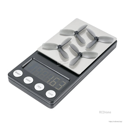 Four grey three-blade propellers placed on a digital scale, showing weighing setup