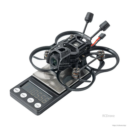 BetaFPV, Small ducted FPV cinewhoop drone with front camera and dual antennas sitting on a digital scale reading 105.56 g