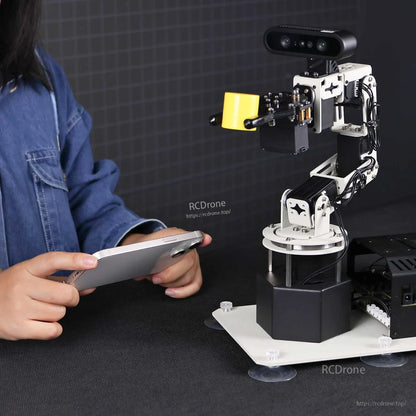 Robotic arm demo holding a yellow block while user controls it from a smartphone at close range