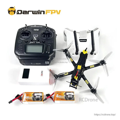 TX12 radio controller and FPV goggles beside quadcopter frame, charger box and two 4-cell batteries on white background