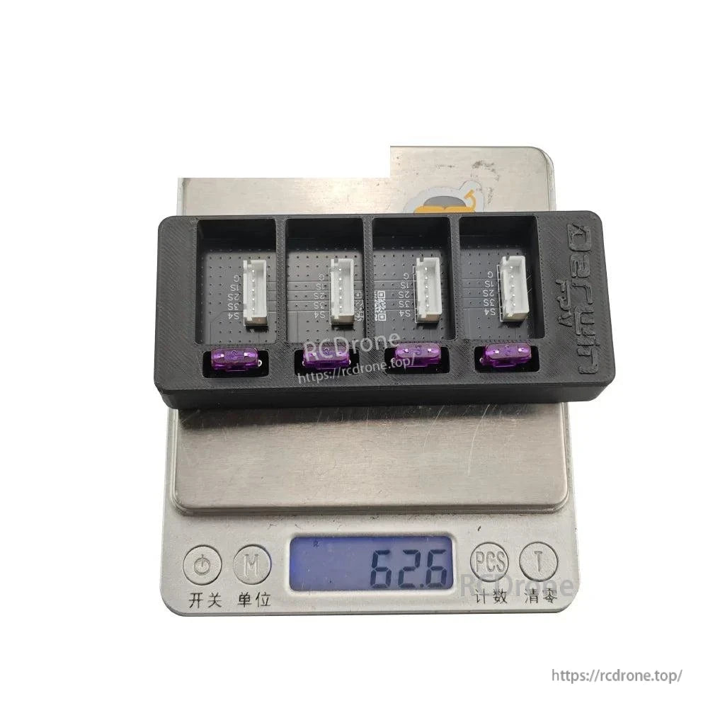 Charger board on digital scale showing weight reading 62.8 g, with four bays and purple fuses