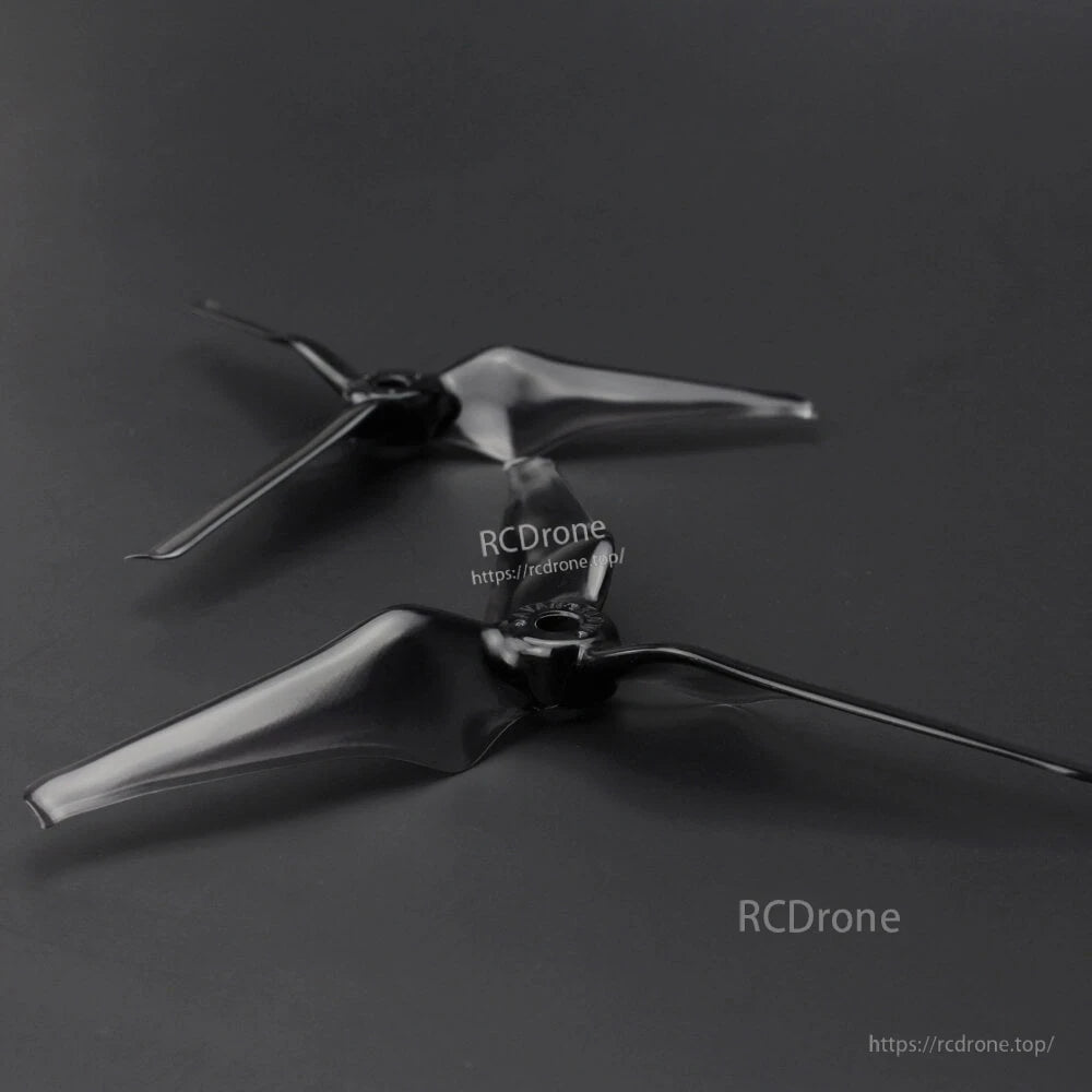 Two black three-blade drone propellers laid on dark background, angled view