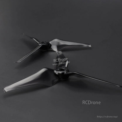 Two black three-blade drone propellers laid on dark background, angled view