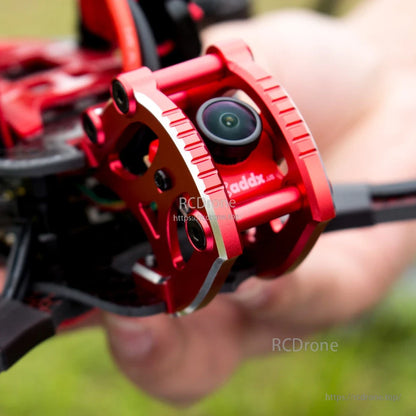Close-up of red aluminum FPV camera cage with lens mounted on the drone frame