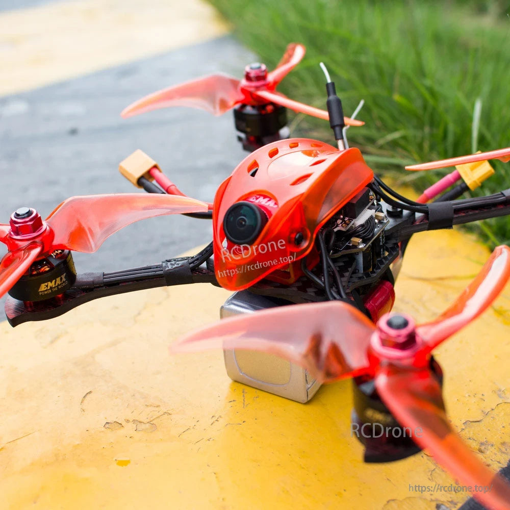 Outdoor angled view showing quad on yellow surface with exposed electronics, battery lead, and camera canopy