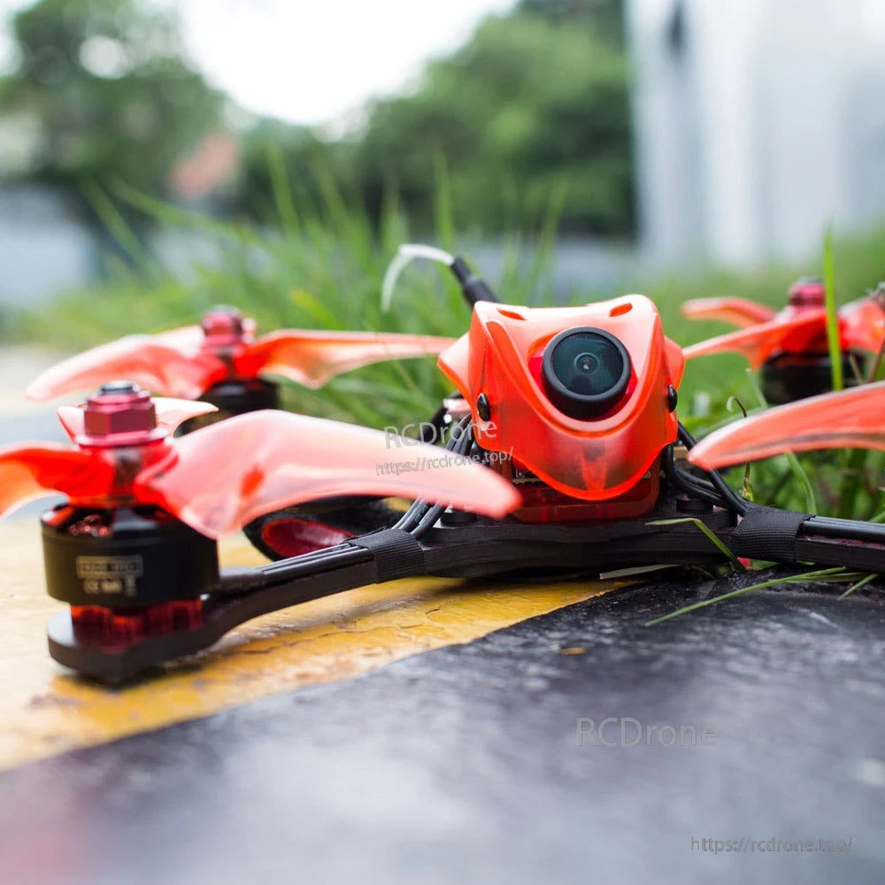 Outdoor close-up on pavement showing the FPV camera lens and front canopy with props in foreground