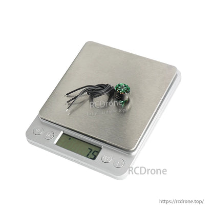 Small Flashhobby A1106 brushless drone motor with three wires sitting on a digital scale reading 7.5 g