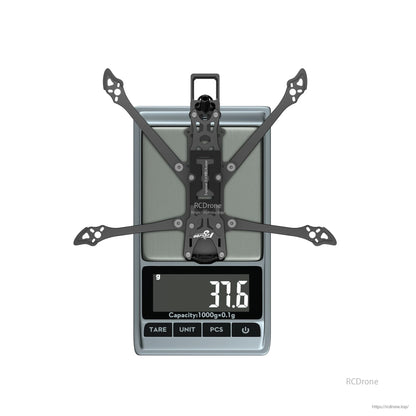 Flywoo Explorer LR4 drone frame kit on a digital scale, showing 37.6g weight with wide carbon arms