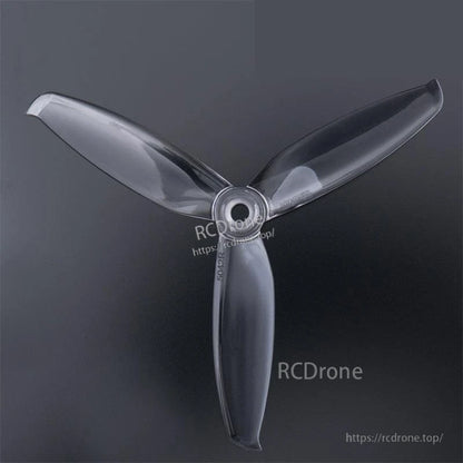 Clear 3-blade drone propeller top view with hub bore visible (watermarked RCDRone)