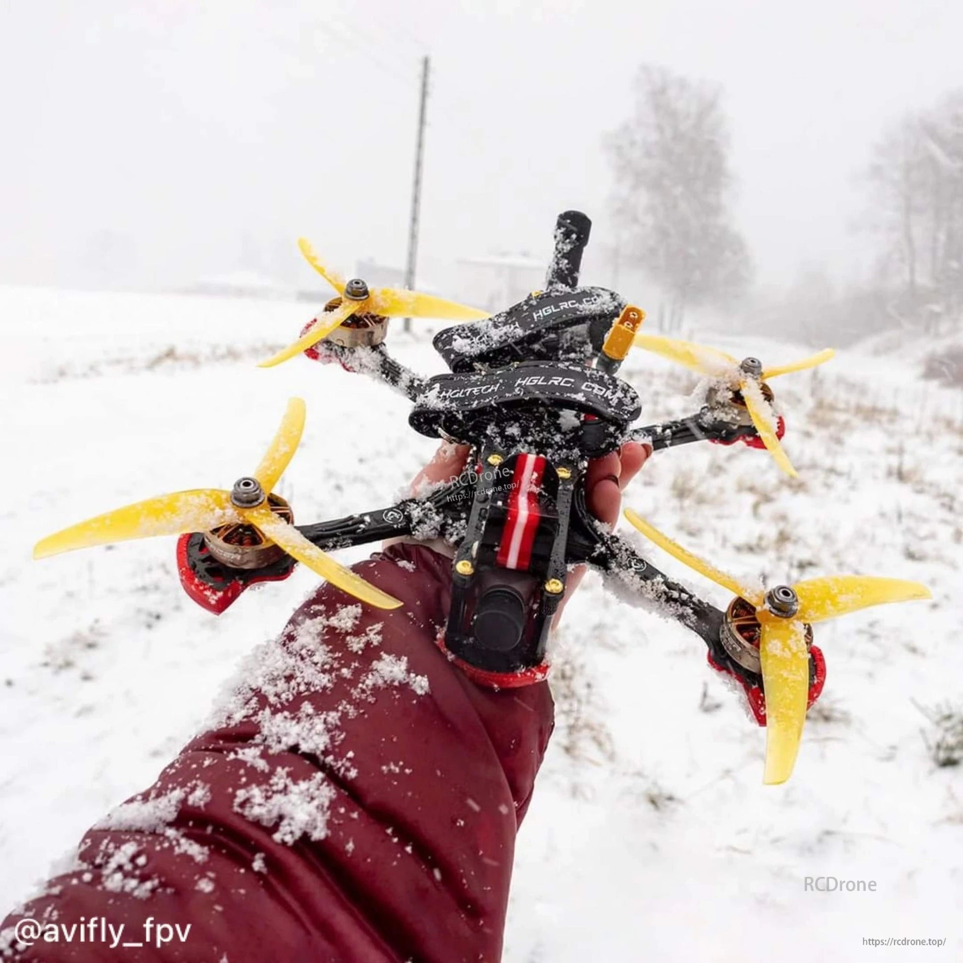 FPV quadcopter with yellow 3-blade propellers held outdoors in snowy weather