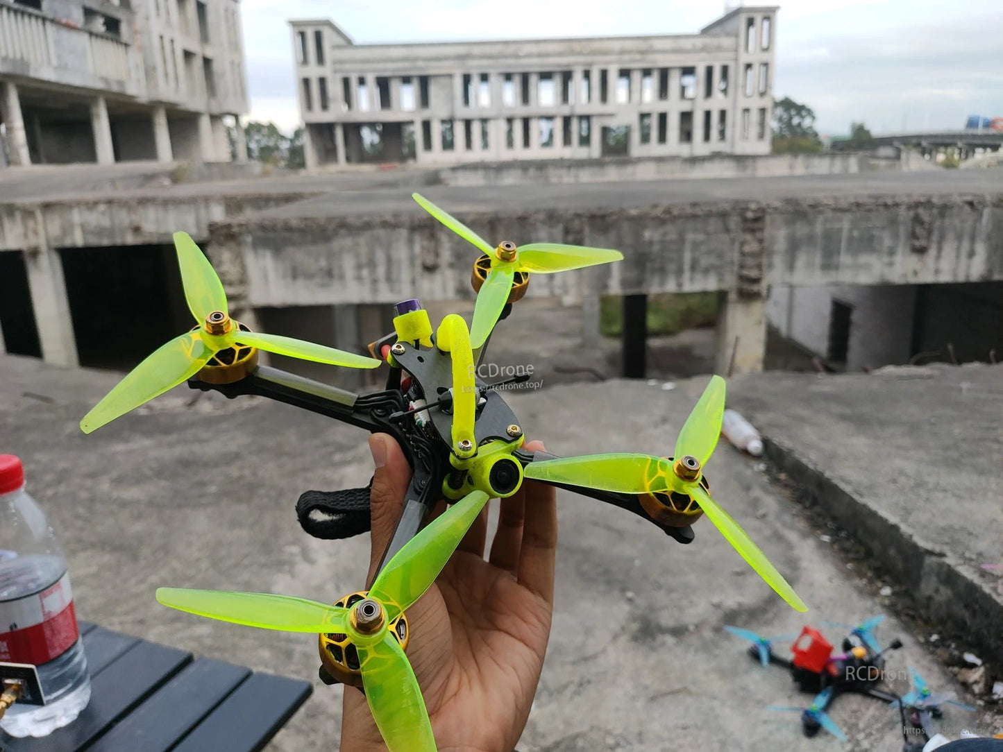 Quadcopter drone fitted with neon green tri-blade propellers, handheld outdoor scene