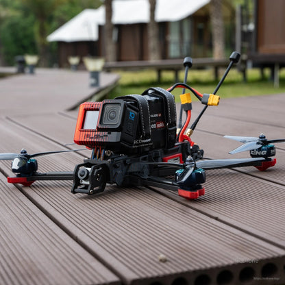 FPV quadcopter on outdoor wooden deck with tri-blade propellers fitted, action camera mounted on frame