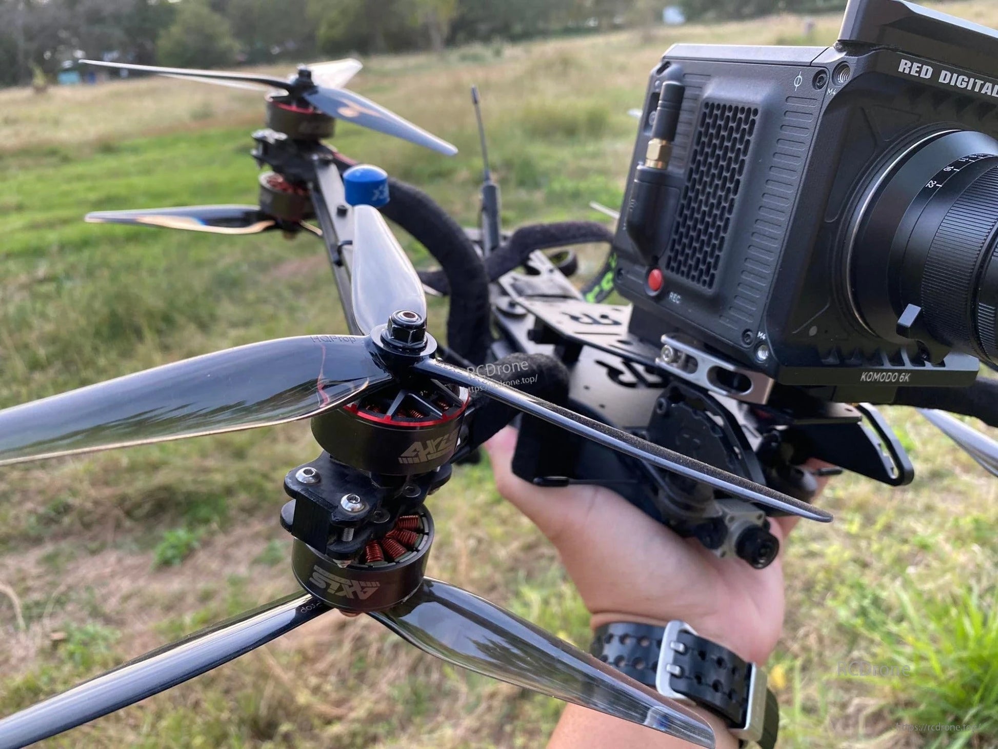 Grey 3-blade propeller installed on a quadcopter drone in outdoor field, close-up on motor mount