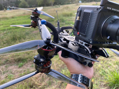Grey 3-blade propeller installed on a quadcopter drone in outdoor field, close-up on motor mount