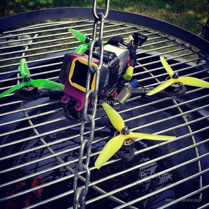 FPV quadcopter fitted with lemon-lime green and yellow 3-blade propellers on motors, outdoor close-up