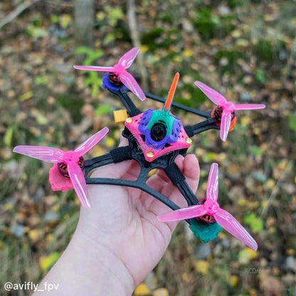 Handheld FPV quadcopter with translucent pink tri-blade propellers, outdoor background