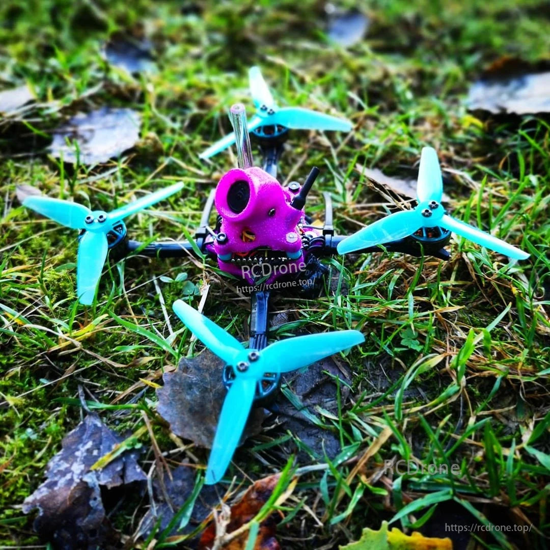 Blue 3-blade propellers installed on a small FPV quadcopter sitting on grass and rocks