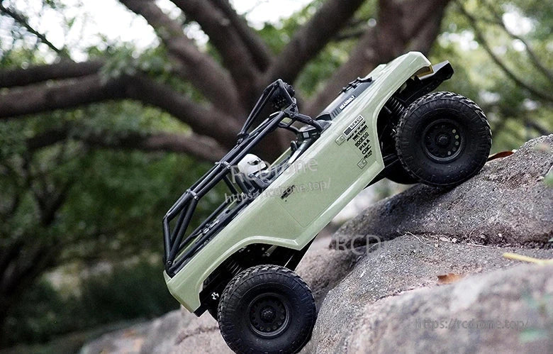 ISDT ESC, RC rock crawler truck climbing over a large rock outdoors, with olive green body panels and roll cage