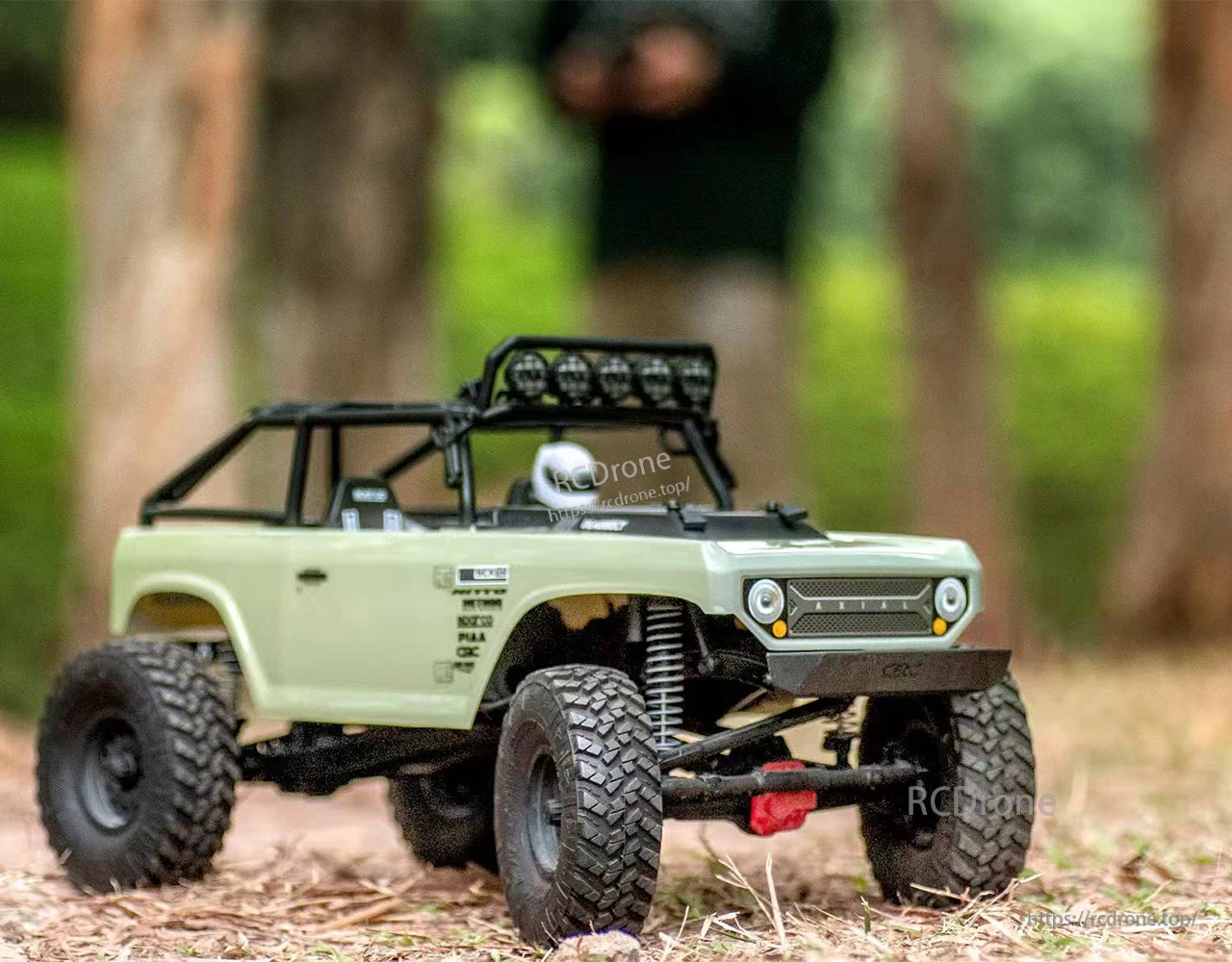 ISDT ESC, Axial RC rock crawler truck with green body, roof light bar, and knobby tires on a dirt trail