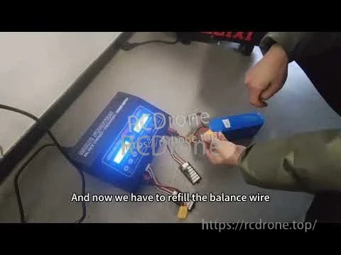 Person handling a blue drone lithium battery pack on a workbench with a balance lead and connector attached