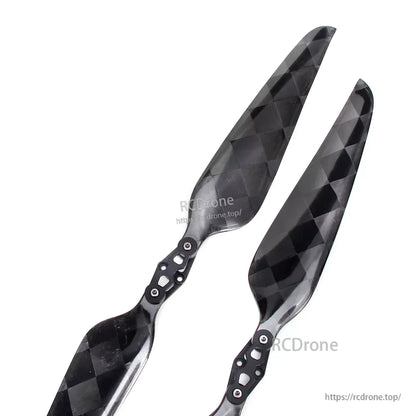 Pair of glossy carbon fiber folding propeller blades with black checker pattern and metal hinge hub