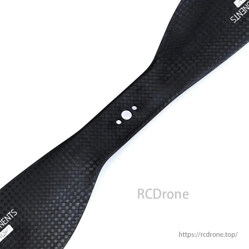 A black carbon fiber part, with a textured surface and small holes, is shown against a white background.