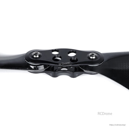 Glossy black carbon fiber folding propeller with metal hub plate, mounting holes, and screws close-up