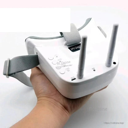 Handheld close-up of FPV goggles showing dual antennas, control buttons, and charging/AV ports
