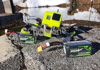 Two OVONIC 1550mAh 4S 14.8V 100C LiPo batteries beside a freestyle FPV drone with action camera mount