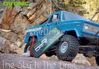 Ovonic 2S hardcase LiPo battery leaning against a blue RC crawler truck on rocky terrain