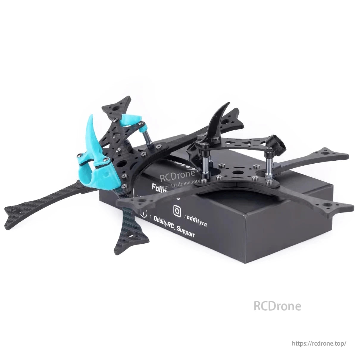 Angled view of FPV drone frame on box showing blue and black TPU accessories and carbon arm cutouts