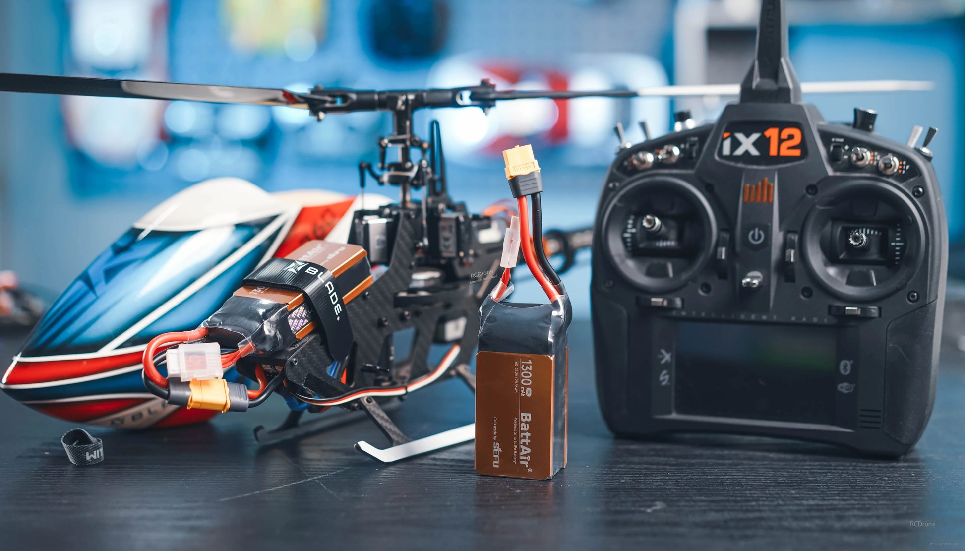 RC LiPo battery pack with XT60 connector and balance lead next to a remote-control helicopter and transmitter