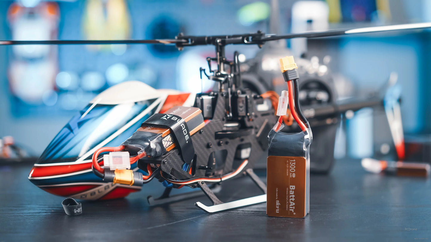 RC LiPo battery pack with 1300mAh label, XT60-style connector and balance lead beside a remote-control helicopter