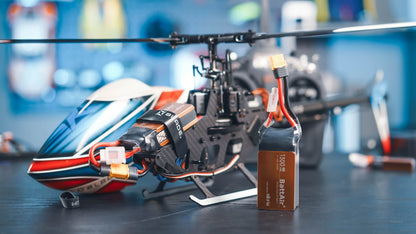 RC LiPo battery pack with 1300mAh label, XT60-style connector and balance lead beside a remote-control helicopter