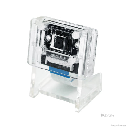 Camera module installed in clear acrylic protective bracket and stand, angled view with ribbon cable
