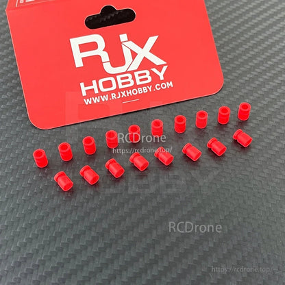 RJX 100pcs 3x5x7mm Damping Ball, RJX Hobby red damping ball bushings for RC models, small cylindrical vibration-damping inserts on a carbon-look surface