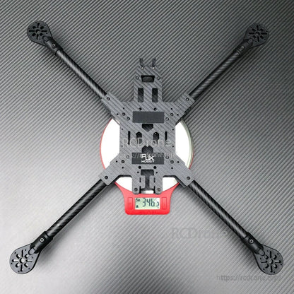 RJX carbon fiber FPV quadcopter frame kit with long arms in X layout, resting on a digital scale