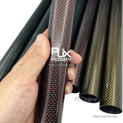 Hand holding RJX 3K carbon fiber tube with woven red-and-black finish, with other carbon tubes in background